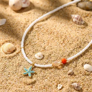 Detailansicht einer Bohème-Halskette mit blauem Seestern-Anhänger auf feinem Sandstrand