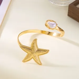 Dettaglio di un bracciale da braccio dorato con stella marina e perla barocca stile mare.