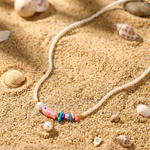 Boho-Sommerhalskette mit rosa Keramikfisch und bunten Perlen im Sand am Strand