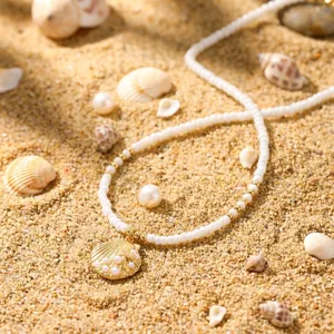 Detailaufnahme einer weißen Perlenkette mit goldenem Muschel-Anhänger auf Sand