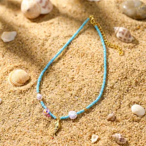 Nahaufnahme einer blauen Perlenkette mit goldenem Muschelanhänger auf Sandhintergrund