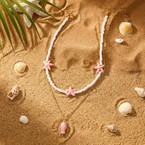 Detailansicht der böhmischen Halskette mit rosa Seesternen und Fisch auf Sand