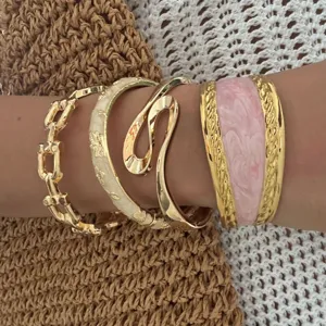 Detailed macro shot of stacked gold bracelets featuring pink and cream enamel finishes.