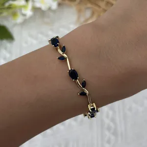 Detail shot of a dainty gold-plated vine bracelet with elegant blue stones on wrist.