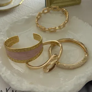 Close-up of light luxury gold bangle set featuring pink enamel and vintage patterns