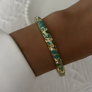 Vintage enamel bangle bracelet with green floral patterns and crystal accents on wrist