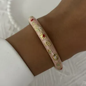 Vintage pink enamel bangle with delicate golden floral patterns on model's wrist