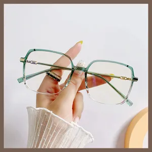 Eleganti occhiali grandi anti-luce blu con montatura sfumata verde tenuti in mano.