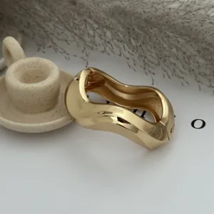 Macro detail of a modern wavy gold alloy bangle featuring a high-polished metallic finish.