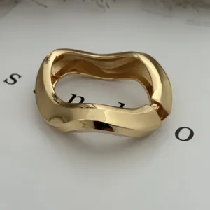 Detailed view of glossy gold-tone wavy alloy bracelet with irregular geometric design.