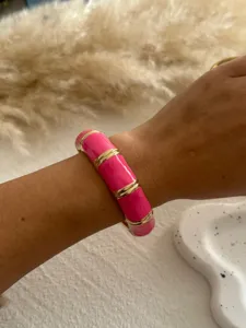 Detail shot of a vibrant pink enamel bangle with gold accents on a model's wrist.