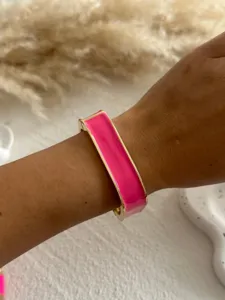 Close-up of a pink enamel bangle bracelet with gold-tone edges worn on a wrist.