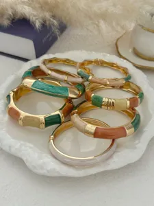 Detail view showing colorful bohemian enamel drip oil bangles on a white ceramic plate