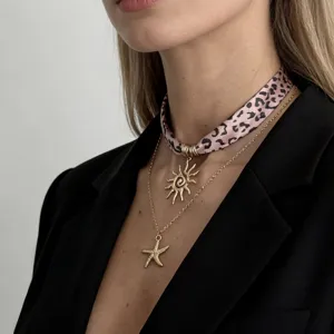 Detail view of pink leopard print silk scarf necklace with gold sun and starfish pendants