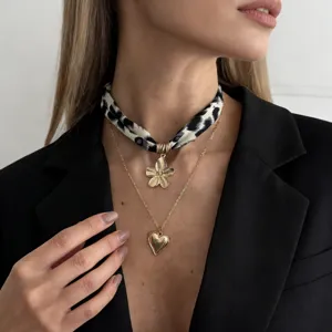 Close-up of a leopard print scarf choker and gold heart pendant necklace on a model.