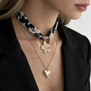 Close-up detail of layered gold necklaces with heart pendant and leopard print scarf