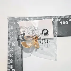 Nahaufnahme eines goldenen Schleifenrings in transparenter Verpackung mit Skalenlineal