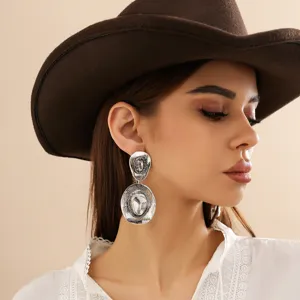 Close-up of vintage silver cowboy hat drop earrings worn by a model in a western outfit.