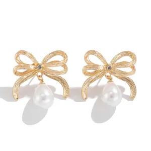 Detailaufnahme eleganter goldener Schleifenohrringe mit hängenden weißen Tropfenperlen