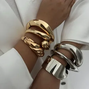 Detailweergave van dikke goud- en zilverkleurige metalen armbanden om de pols van een model