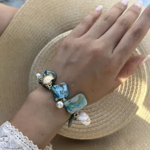 Detailansicht eines Ozean-Armbands mit blauen Muscheln und Perlen an einem Handgelenk.