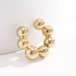 Dettaglio macro di un ear cuff a sfere dorate minimalista con finitura lucida a specchio