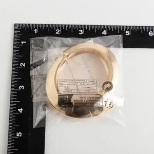 Gedetailleerd overzicht van een gouden metalen armband in verpakking naast een liniaal