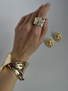 Primer plano de un brazalete dorado con textura arrugada y un anillo grande a juego.