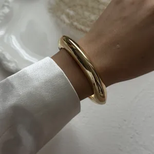 Detailed view of a thick polished gold alloy teardrop bangle worn on the wrist