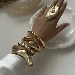 Close-up detail of stylish chunky gold-plated bangles and a large pearl ring.