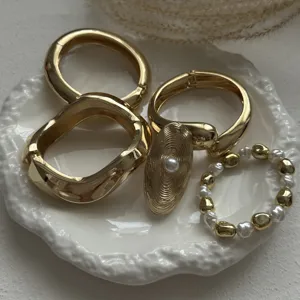 Detailed shot of elegant textured gold alloy bangles and pearl ring on white ceramic dish