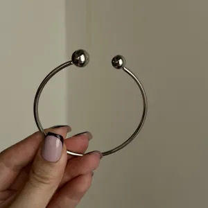 Primo piano di un bracciale rigido argento minimalista con doppie estremità a sfera.
