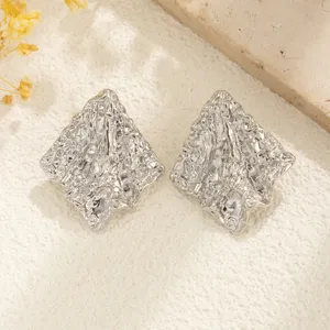 Detalle macro de pendientes plateados con textura arrugada y forma de rombo geométrico