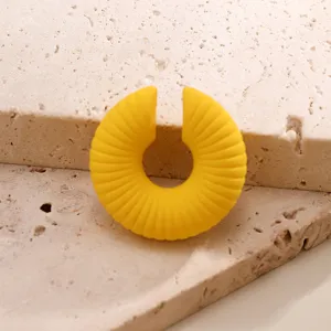 Dettaglio di un ear cuff a coste giallo vivace su uno sfondo in pietra naturale