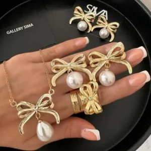 Elegantes goldenes Schleifen-Schmuckset mit weißen Perlenimitaten auf einer Hand.