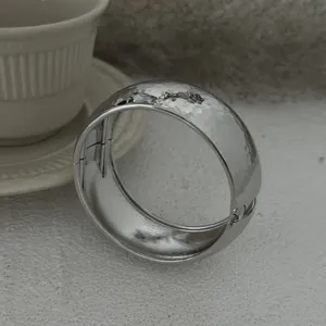 Detailansicht eines silberfarbenen Metall-Klapparmreifs mit einer Hammerschlag-Textur.