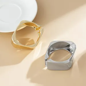 Nahaufnahme von gold- und silberfarbenen unregelmäßigen quadratischen Armreifen auf Beige.
