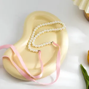 Close-up of vintage pearl necklace with elegant pink ribbon ties on a display tray