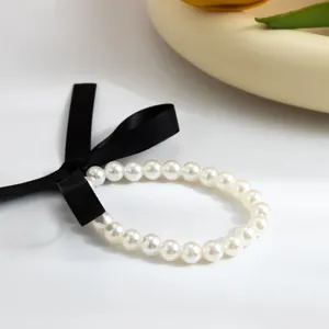 Close-up detail of a retro pearl choker featuring a black ribbon bow and glossy white pearls.