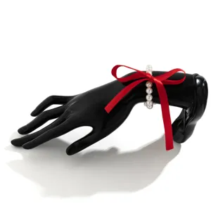 Elegant red ribbon bow choker with white pearls on a black display hand
