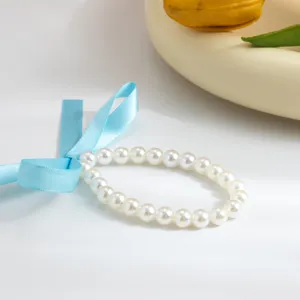 Close-up detail of an elegant white pearl necklace featuring a soft blue satin ribbon bow.