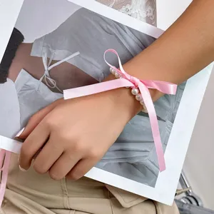 Detail view of a versatile pearl accessory with a pink satin ribbon bow tied on a wrist