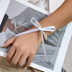 Close-up of an elegant pearl bracelet with a white ribbon bow worn on a female wrist