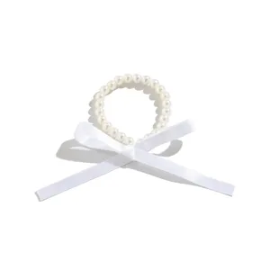 Detail view of a vintage pearl choker featuring a delicate white satin ribbon bow tie.
