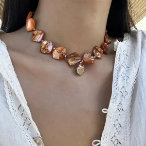 Nahaufnahme der schillernden orangefarbenen Muschelkette mit goldenem Muschelanhänger