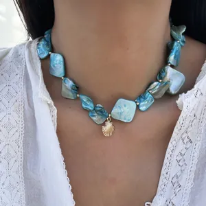 Nahaufnahme einer blauen Halskette aus Steinen mit einem goldenen Muschelanhänger.