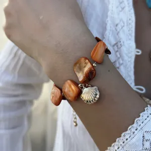 Detailansicht eines Ozean-Armbands mit orangen Steinen und einem goldenen Muschel-Anhänger