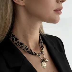 Close-up of leopard print silk scarf necklace with gold heart pendant on model