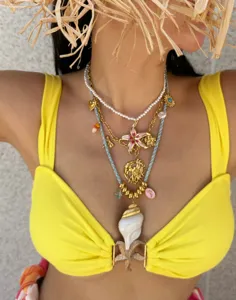 Close-up of layered vintage 14k gold necklaces with seashell and sun pendants on a model.