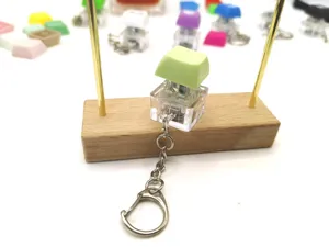 Close-up of a green mechanical keycap switch keychain on a wooden stand